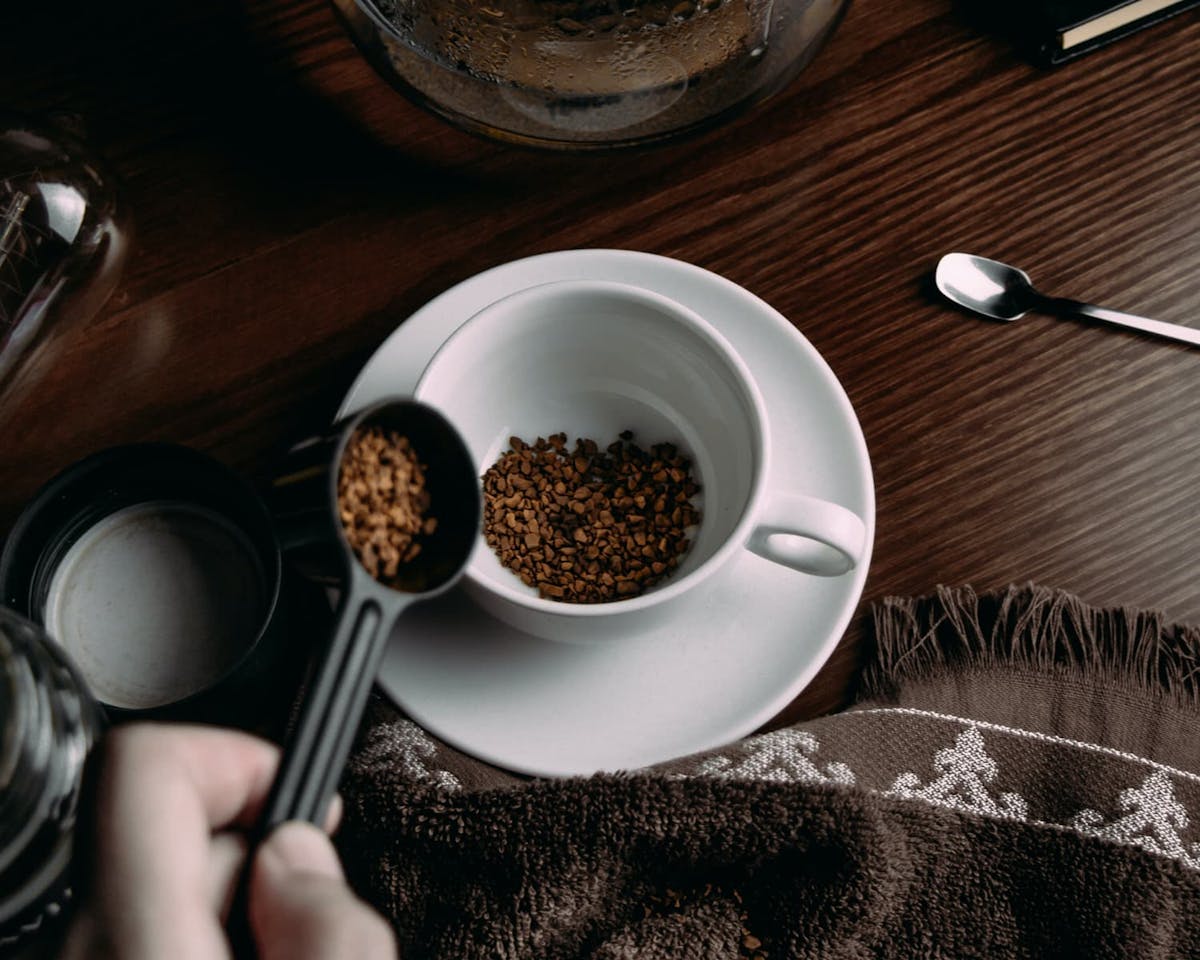a person scooping instant coffee into a coffee mug.